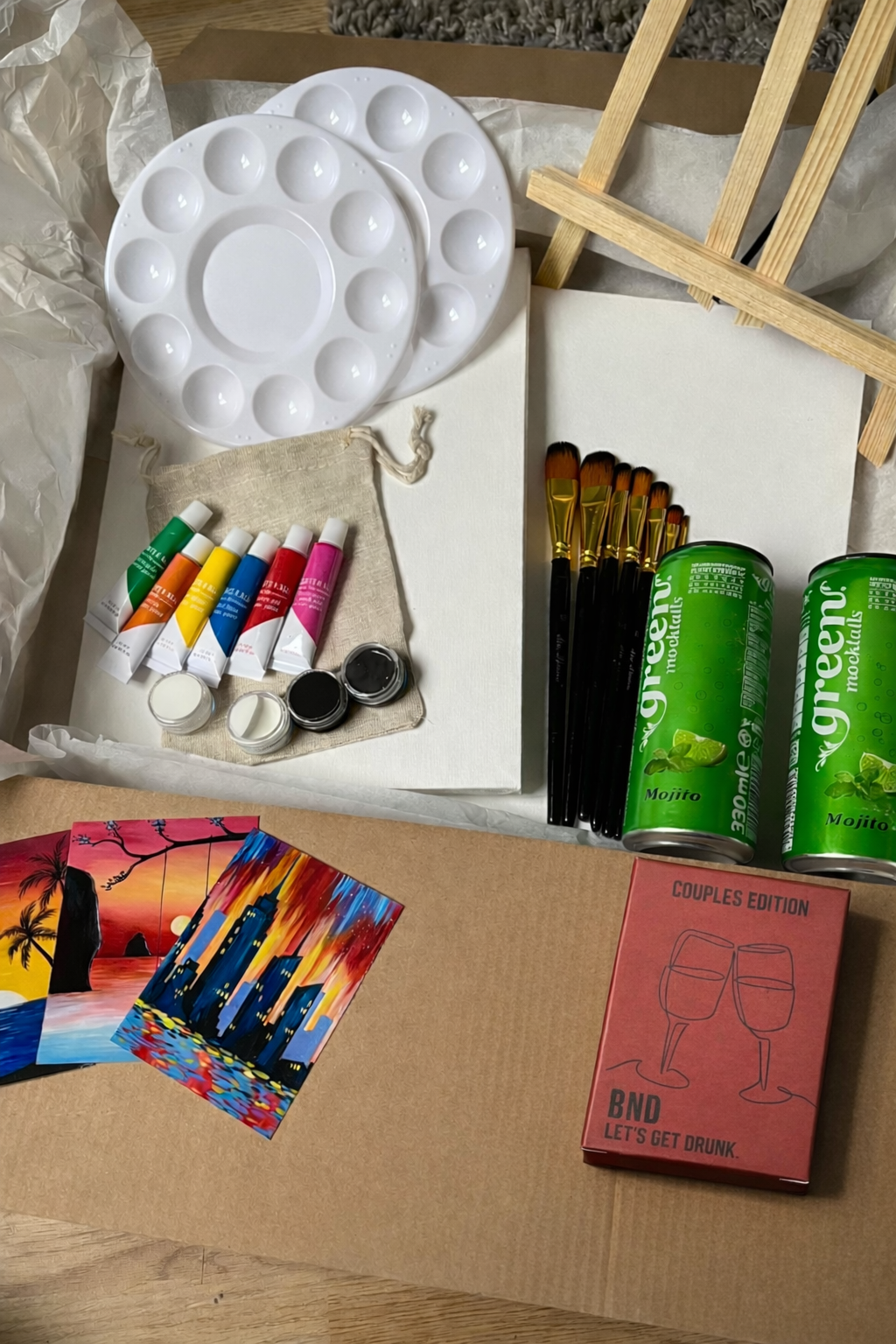 Art supplies including a paint palette, brushes, and paint tubes on a cardboard surface.