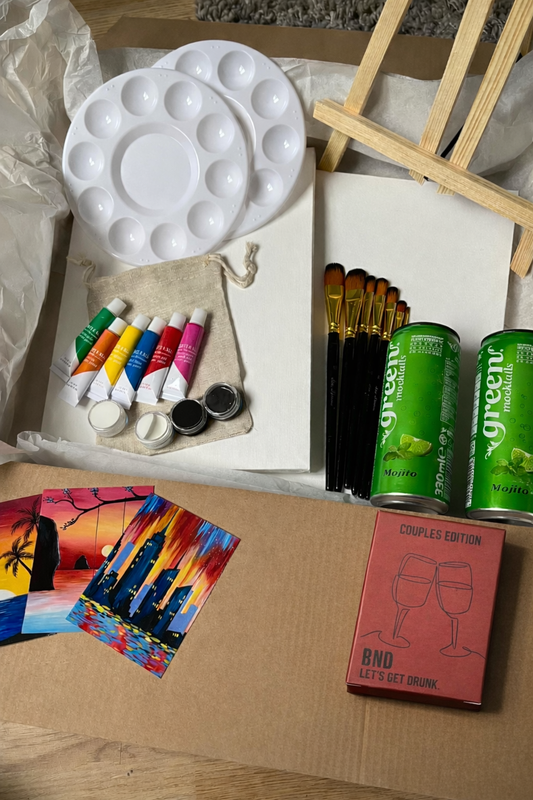 Art supplies including a paint palette, brushes, and paint tubes on a cardboard surface.