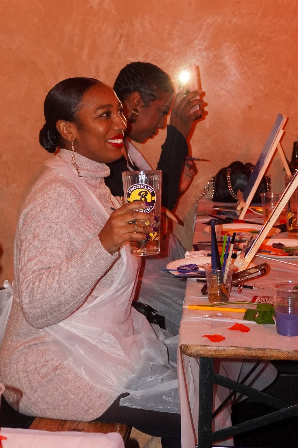 Two people sitting at a table with drinks and a laptop, taking a selfie.